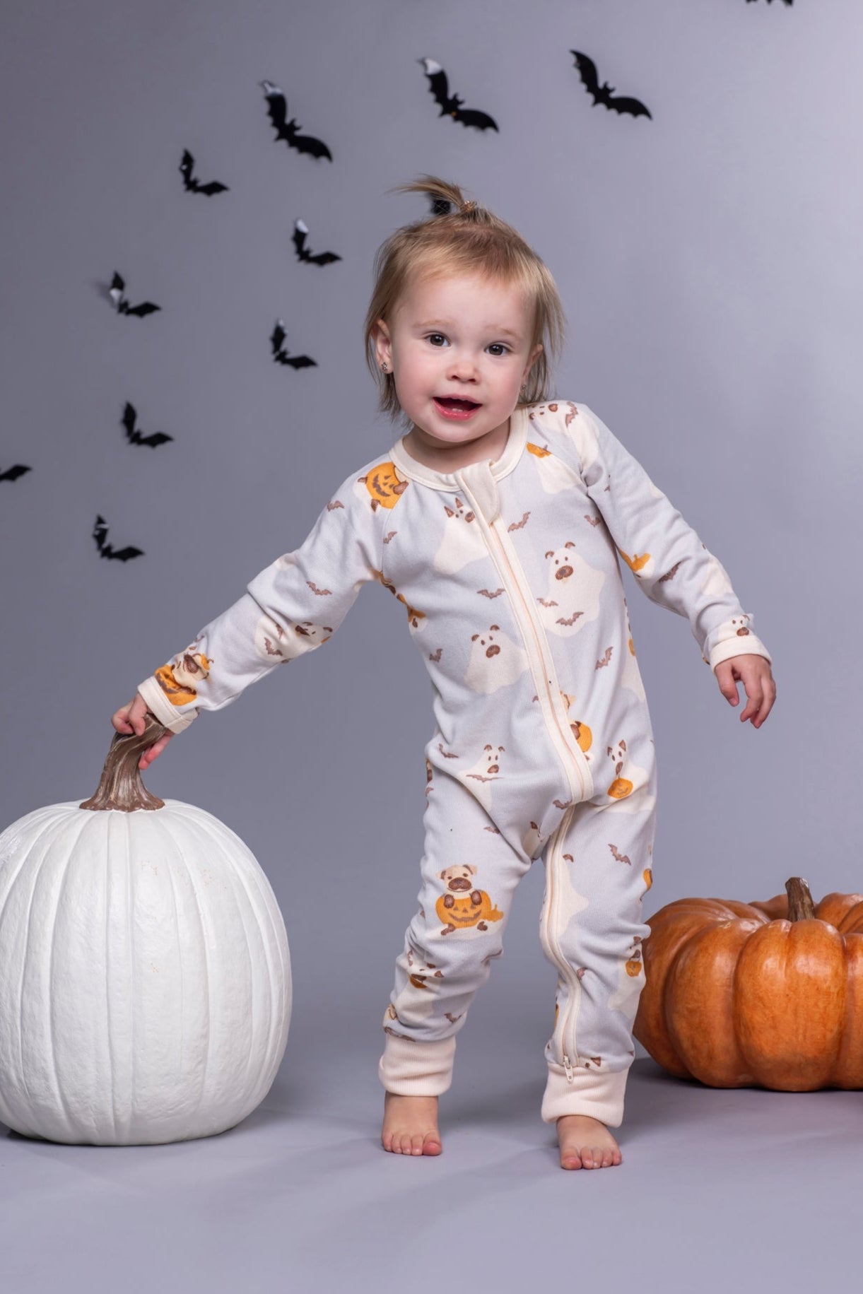 Child in Halloween-themed pajamas with pumpkins and bats on a gray background