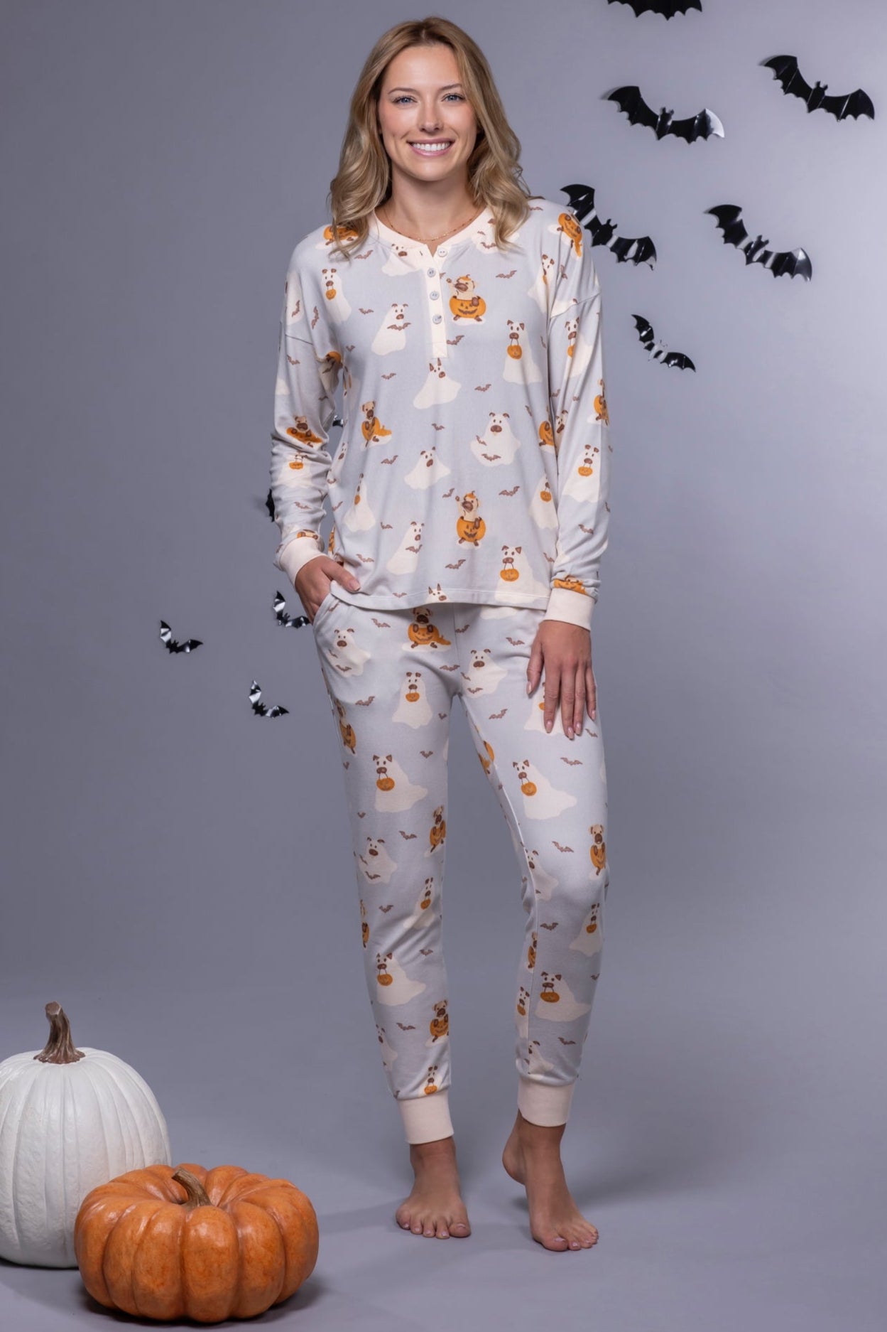 Woman wearing Halloween-themed pajamas with pumpkins and bats on a gray background.