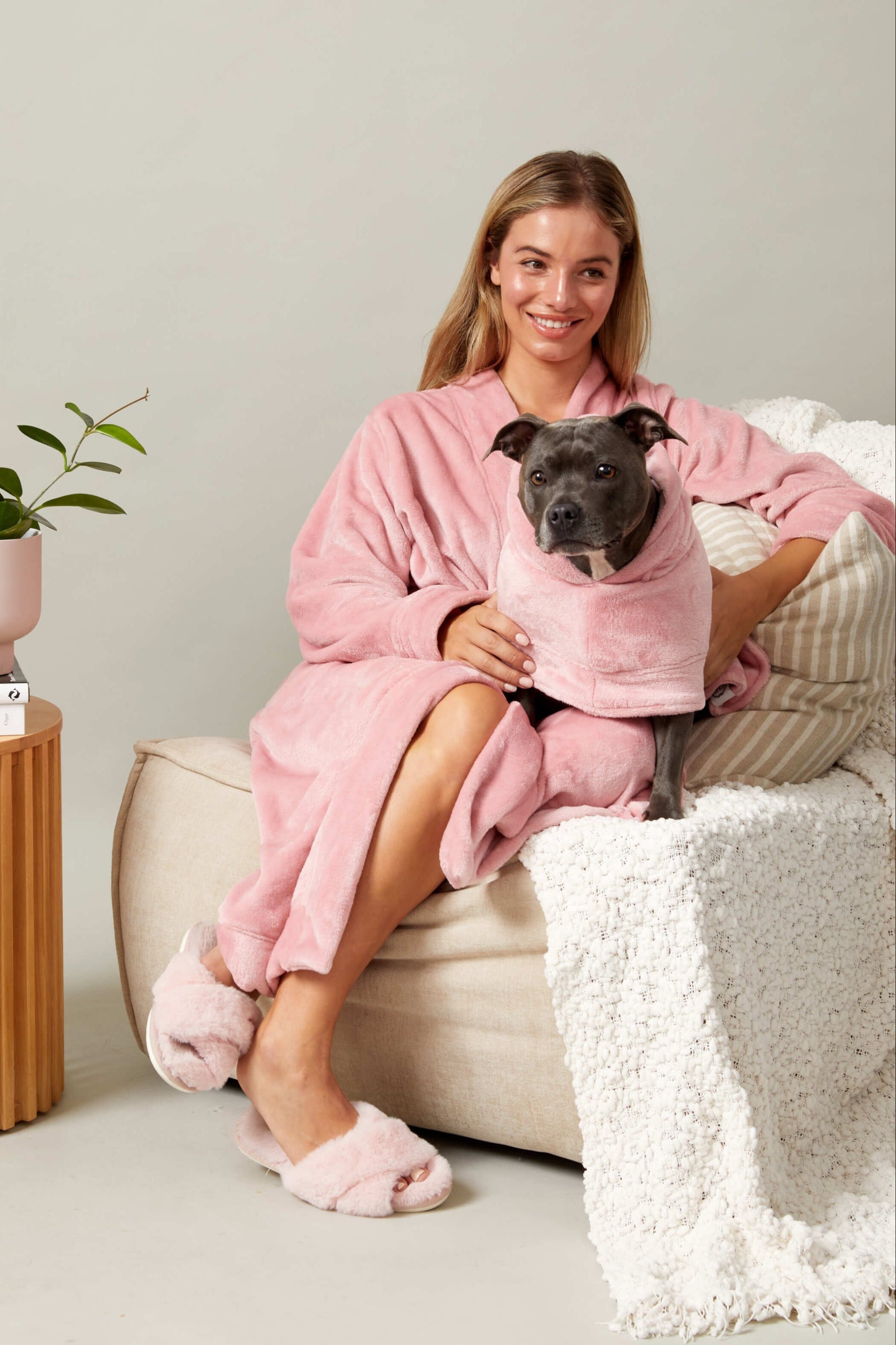 A women cuddling her dog on the couch wearing match your dog pink fluffy robes.