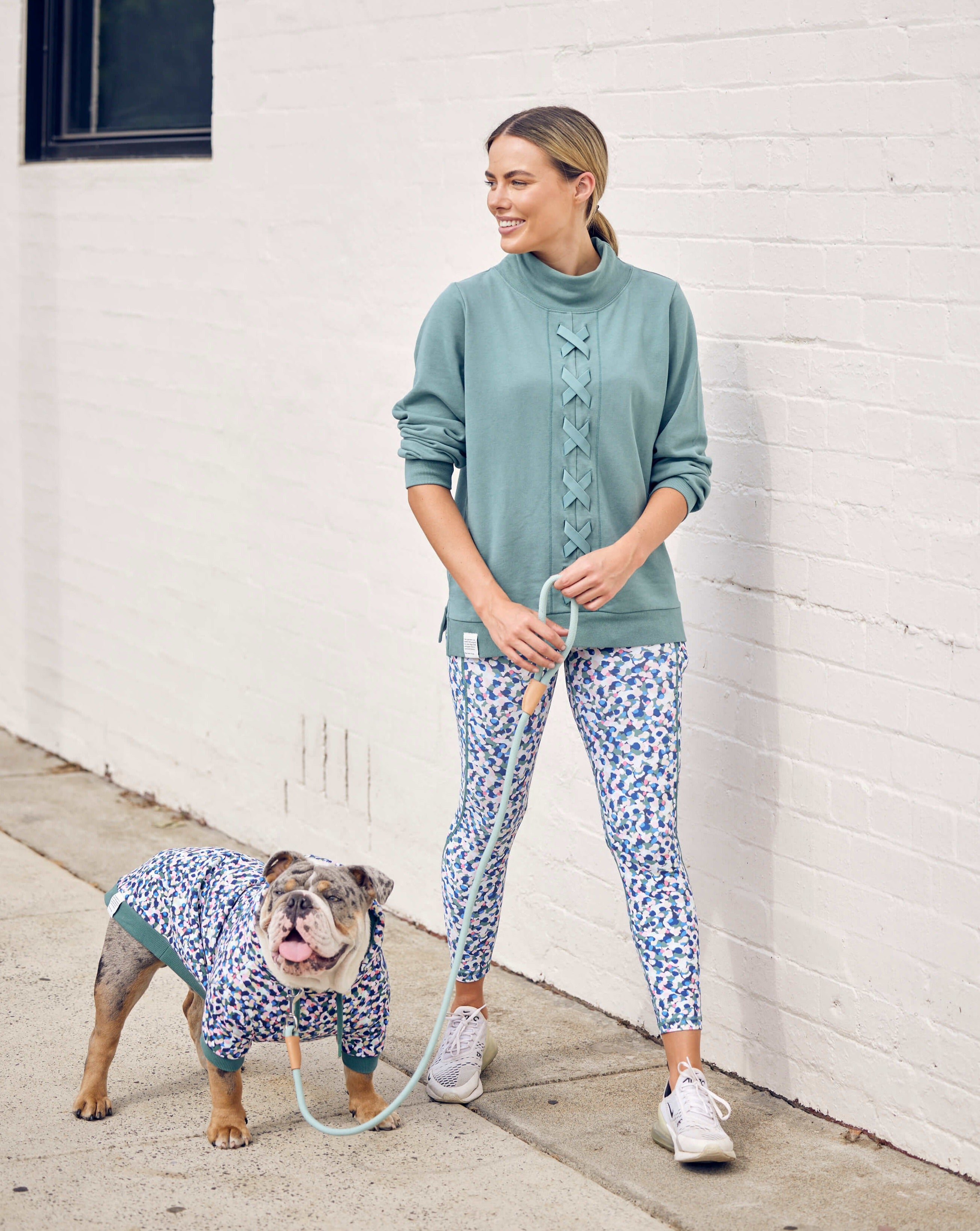A lady walking her Bulldog wearing matching Darren and Phillip dog hoodie and leggings.