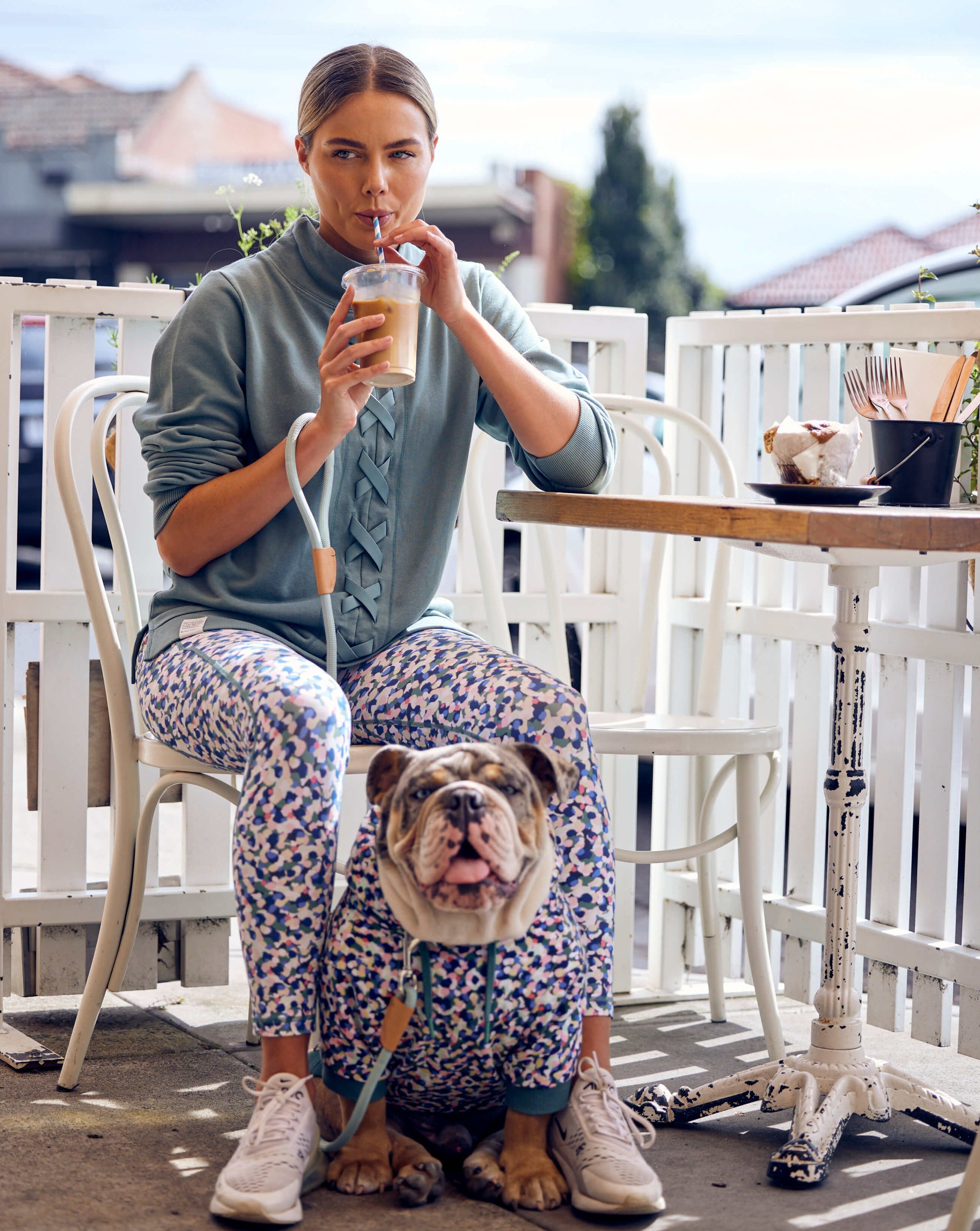 A lady and her bulldog sitting at a cafe wearing match your dog hoodie and leggings from Darren and Phillip.