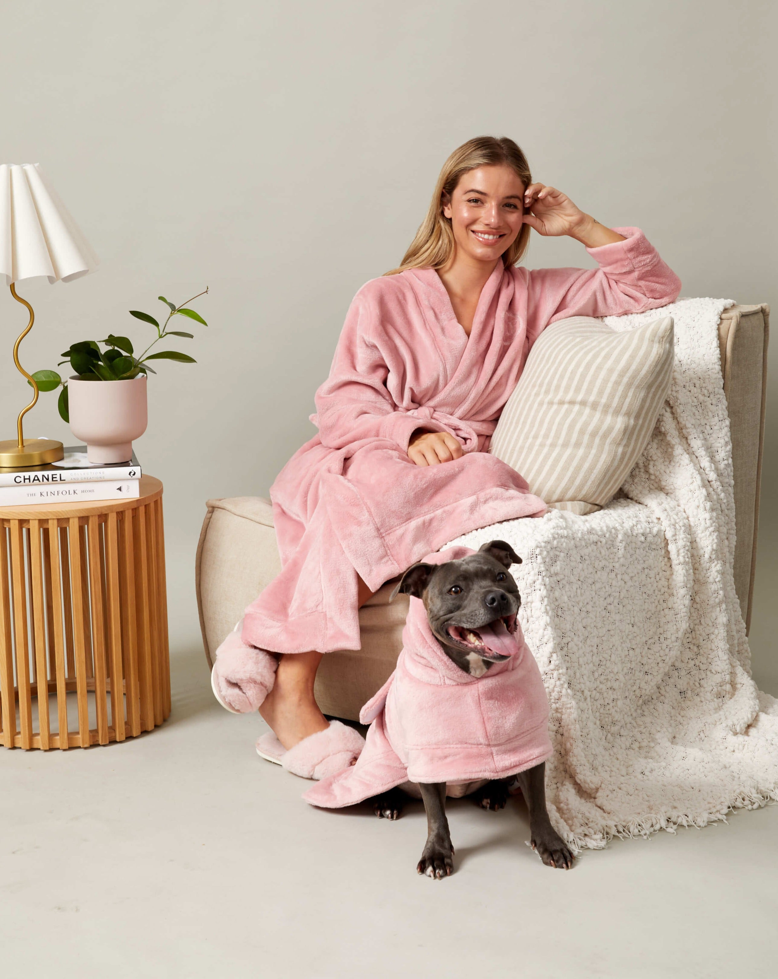 A smiling woman and her Staffy wearing matching dog and human robes in pink.