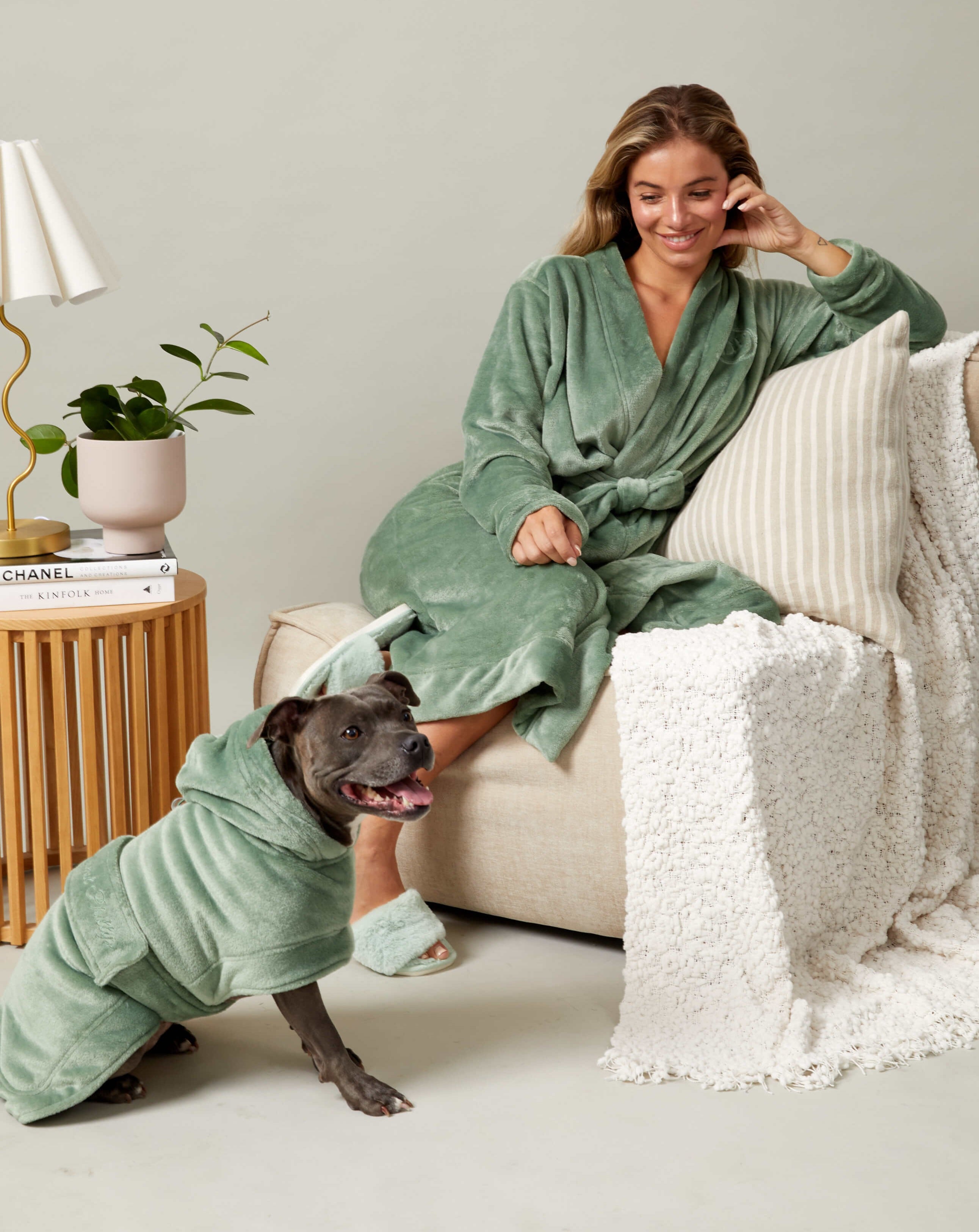 A woman and a dog relaxing at home wearing matching human and dog fluffy robes.